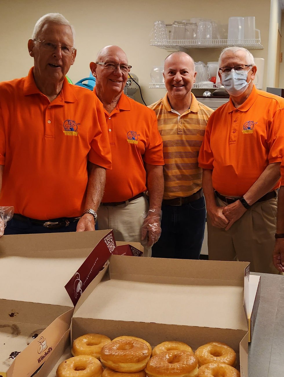 A group of men in orange shirts giving donuts
