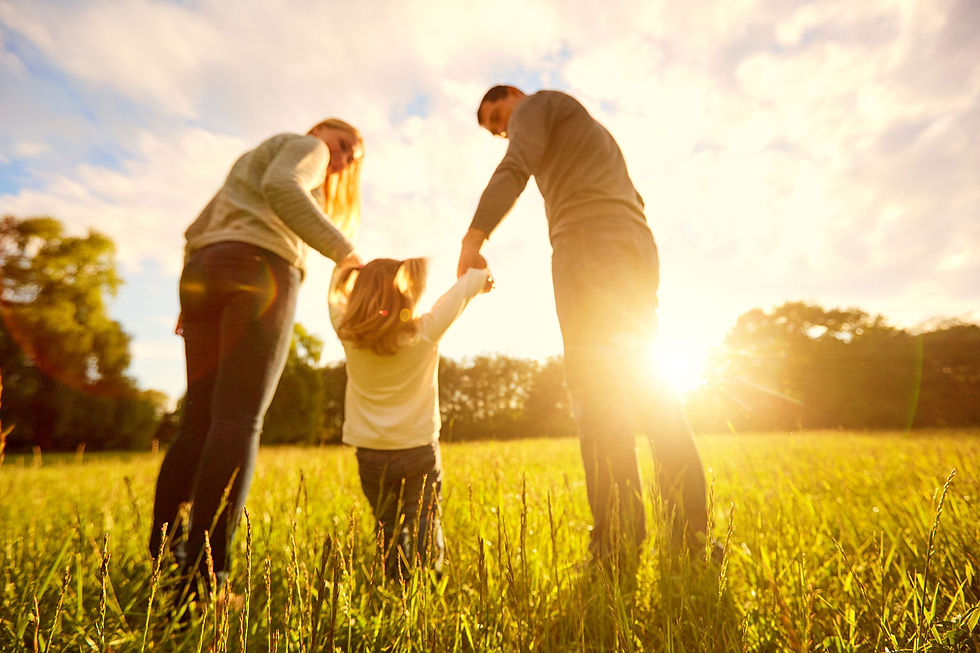 A family holding hands with their toddler in a sunny field